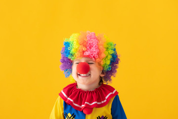 Funny kid clown playing against yellow background