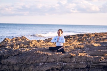 Young beautiful sportwoman smiling happy practicing yoga. Coach with smile on face teaching prayer pose at the beach