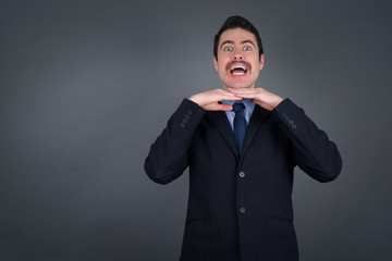 Pretty surprised businessman fooling around in studio and jumping. Adorable guy dancing on colorful background and touching chin with hands having good time.
