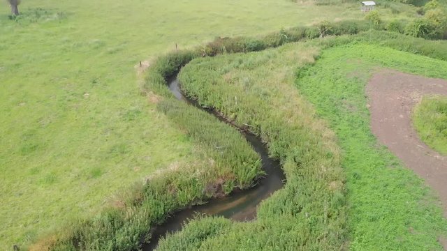 Aerial view move forward of a small river and its meander betwin field and pasture