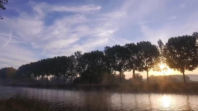 Sunrise on the schelde river with fog on the water and the sun behind the threes