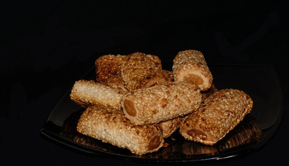 Cookies in the form of tubes with filling. sprinkled with sesame seeds. On a black background