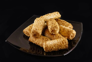 Cookies in the form of tubes with filling. sprinkled with sesame seeds. On a black background