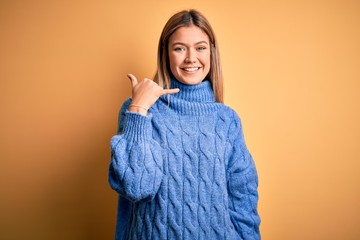 Young beautiful blonde woman wearing turtleneck sweater over yellow isolated background smiling doing phone gesture with hand and fingers like talking on the telephone. Communicating concepts.