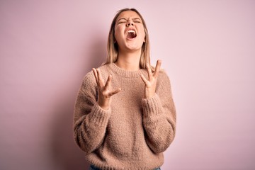 Young beautiful blonde woman wearing winter wool sweater over pink isolated background celebrating mad and crazy for success with arms raised and closed eyes screaming excited. Winner concept