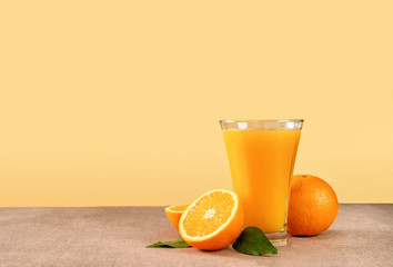 Glass of orange juice with oranges on light yellow background