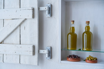 Two beautiful bottles of cooking oil or fresh olive oil stand on a white shelf above two shells of olive, rural Mediterranean living space in a kitchen in Spain