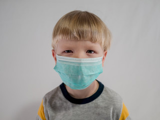 Funny blond kid in green medical mask to protect against influenza viruses in crowded places. China Wuhan coronavirus