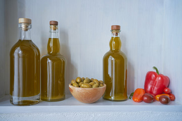 three bottles cooking oil and a wooden bowl with green olives next to red vegan vegetarian vegetables like tomatoes and paprika in spain