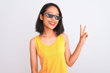 Naklejka premium Young beautiful chinese woman wearing thug life sunglasses over isolated white background smiling with happy face winking at the camera doing victory sign. Number two.