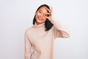 Fototapeta premium Young chinese woman wearing turtleneck sweater standing over isolated white background doing ok gesture with hand smiling, eye looking through fingers with happy face.