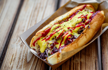 Philly cheese steak sandwich with meat, vegetables, cheese and sause in box on wooden table. street food