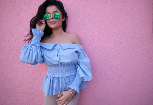 Woman In A Summer Stylish Striped Sundress Rests Near A Pink Vintage Wall In The City. Cute Urban Girl Model Outdoors. Stylish Women Clothes. Summer Style.