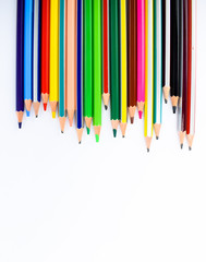 Line of different colored pencil and crayons on a white background facing downwards.