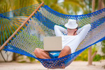 Young man with laptop at hammock on tropical vacation