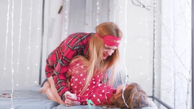 mom and daughter are fooling around in bed in pajamas