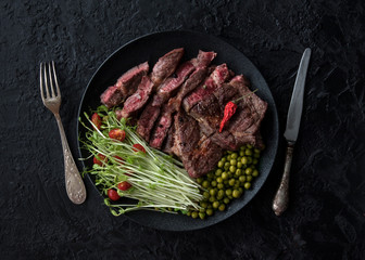 Juicy fried steak with a salad of sprouted peas, green peas and tomatoes on a black background. The healthy concept of separation of power. The view from the top.