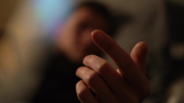 Man in bed beckons with his finger as a gesture or invitation to join him - background bokeh