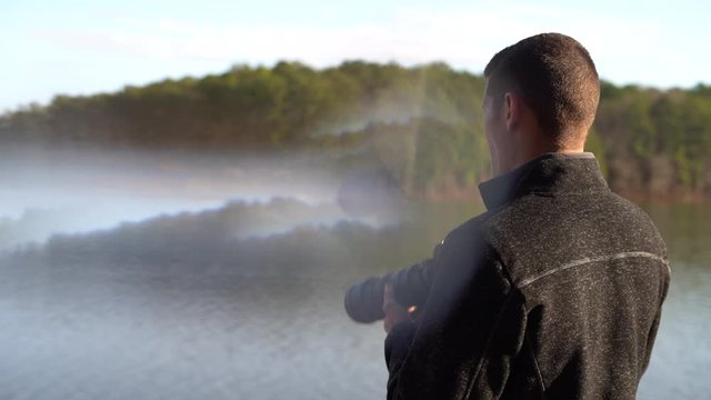 Young male photographer checks the screen on his dlsr camera after taking a picture using a telephoto lens looking over a lake in the forest - stylistic distortion and reflection as seen through glass