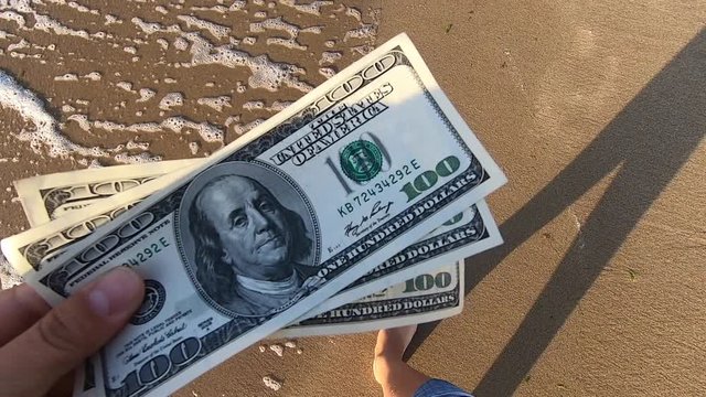 Girl holding money bill of 300 dollars on background of sea ocean waves