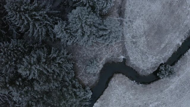 Top down ascending shot, snow covered pine trees, river and landscape in Murnau, Germany.