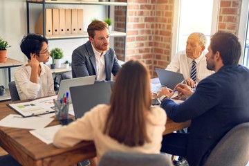 Group of business workers working together. Sitting on desk using laptop and talking at the office
