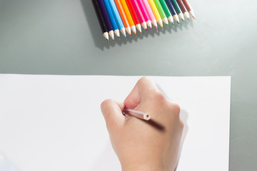 the girl draws on a white sheet of paper with colored pencils