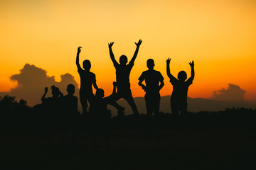 Silhouette group of happy jumping kids under the yellow sunset sky. Concept for happiness and freedom life of young people..