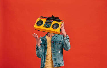 Studio shot of man catching or throwing retro music player, which hiding his face. Isolated on red background