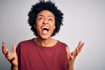 Young beautiful African American afro woman with curly hair wearing casual t-shirt standing crazy and mad shouting and yelling with aggressive expression and arms raised. Frustration concept.