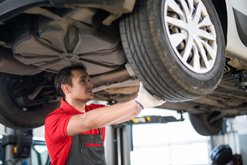 Portrait of a mechanic repairing a lifted car at station