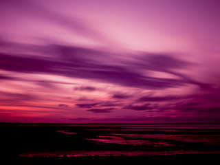Magenta Tinted Sky Over A Pink Beach In Silhouette