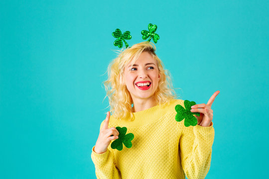 Studio portrait of a smiling woman holding shamrock  having fun and pointing up, with St. Patrick's Day head decoration