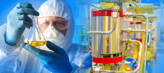 Chemist in a protective suit on the background of a bioreactor. Work of a microbiologist. A man is...