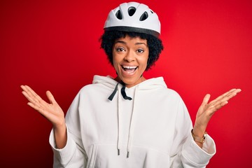 Young African American afro cyciling woman with curly hair wearing bike security helmet celebrating crazy and amazed for success with arms raised and open eyes screaming excited. Winner concept