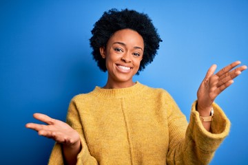 Young beautiful African American afro woman with curly hair wearing yellow casual sweater smiling...