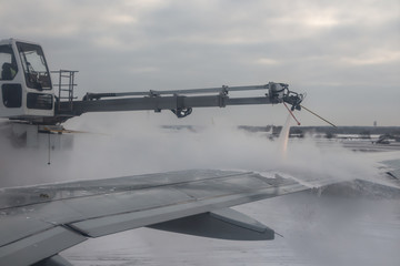 Process of spraying anti-icing white fluid the rear part of the wing of a plane at the airport at...