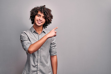 Young handsome eastern man points with finger to your copy space