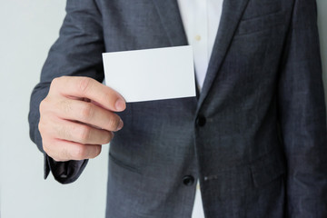 Men business person wearing grey formal suit and white shirt holding Blank white business card mock up template to put name and text on. Advertisement for business concept, contact detail.