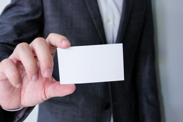 Men business person wearing grey formal suit and white shirt holding Blank white business card mock up template to put name and text on. Advertisement for business concept, contact detail.