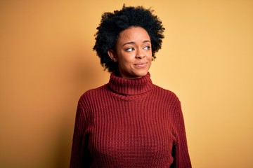 Fototapeta na wymiar Young beautiful African American afro woman with curly hair wearing casual turtleneck sweater smiling looking to the side and staring away thinking.
