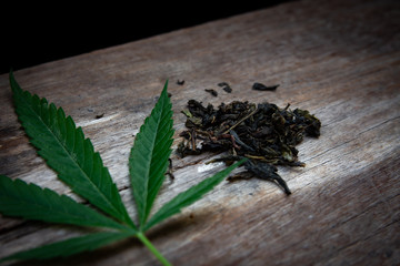 Green marijuana leaves and dried marijuana leaves placed on an old wooden table. Dark tone. 