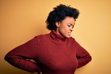 Fototapeta na wymiar Young beautiful African American afro woman with curly hair wearing casual turtleneck sweater Suffering of backache, touching back with hand, muscular pain