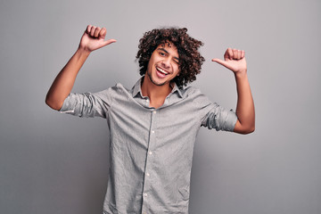 Cool smiling eastern guy shows thumbs up with both hands on isolated gray backround.