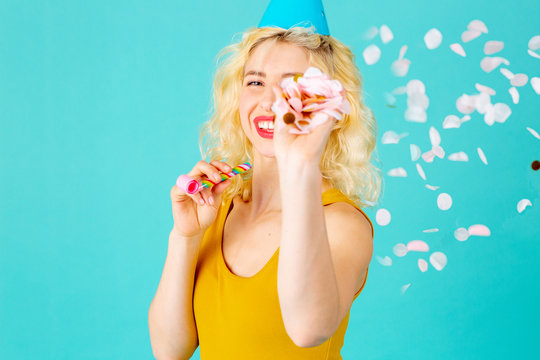 Portrait of a happy, smiling young woman celebrating fun birthday party hrowing confetti, isolated on blue