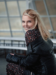 Young happy pretty blond woman in trendy vintage dress and black leather jacket enjoying life posing sitting in gazebo city park