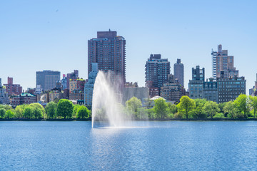 Obraz premium Many fresh green trees and plants grow along the Central Park Reservoir toward to the Central Park East residents in the morning at Central Park at New York City NY USA on May. 06 2019.