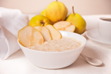 Oatmeal porridge with ripe pears in the white bowl, a bowl of pears and cup of coffee on the background. Health breakfast. Close up.