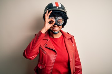 Young African American afro motorcyclist woman with curly hair wearing motorcycle helmet doing ok gesture with hand smiling, eye looking through fingers with happy face.
