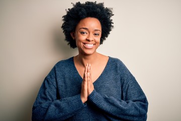 Young beautiful African American afro woman with curly hair wearing casual sweater praying with...